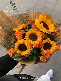 a bouquet of sunflowers and roses is held by someone's hand on the sidewalk