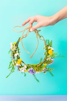 a hand is holding a wreath made out of flowers and twine on a blue background