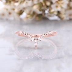 a rose gold ring with three diamonds on it and some flowers in the back ground