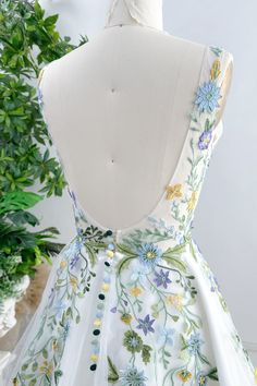 a white dress with blue and yellow flowers is on display in front of a potted plant