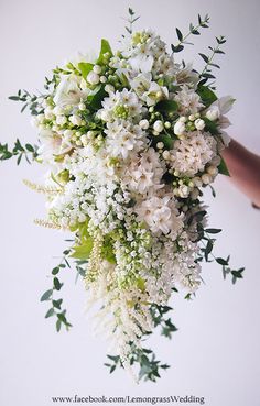 a bouquet of white flowers and greenery is held up by someone's hand