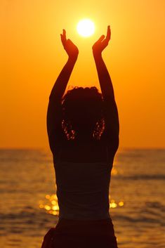 a woman is standing on the beach with her hands in the air as the sun sets