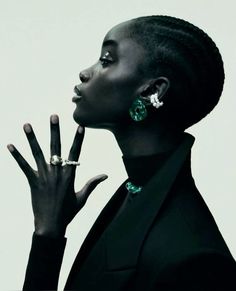 a woman with her hand up to her face, wearing earrings and a black suit