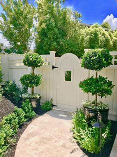 a white gate surrounded by potted trees and shrubbery