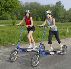 two women riding scooters on the road