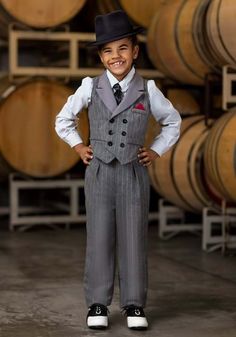 a young boy wearing a suit and tie standing in front of some wine casks