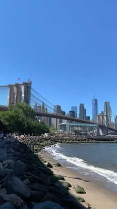 people are walking on the beach in front of the brooklyn bridge and lower manhattan, new york city