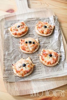 four small pizzas with cheese and black olives on them are sitting on a newspaper