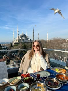 a woman sitting at a table covered in plates of food with a view of the blue mosque