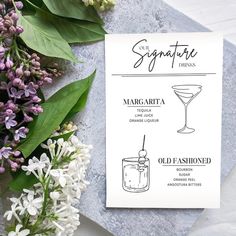 the signature drink menu is displayed next to flowers and greenery on a marble surface