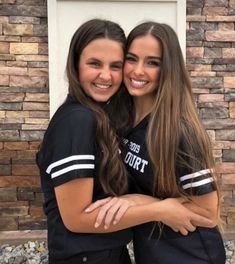 two girls hugging each other in front of a brick wall