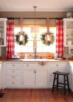 the kitchen is decorated for christmas with wreaths on the windowsill and red curtains