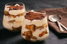 two glasses filled with dessert sitting on top of a table next to a spoon and napkin