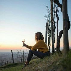 a woman sitting on the side of a hill holding a glass of wine in her hand