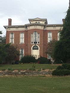 a large red brick building sitting on top of a lush green field next to trees