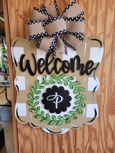 a welcome sign hanging on the side of a wooden door with a wreath and bow