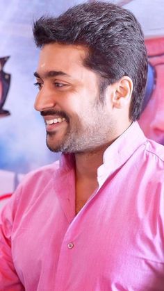 a man in a pink shirt smiles at the camera while standing next to a wall with pictures on it