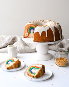 a bundt cake with white icing and rainbow designs on it, next to two slices