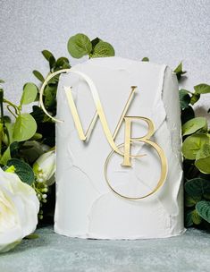 a wedding cake with the initials v and b on it, surrounded by greenery