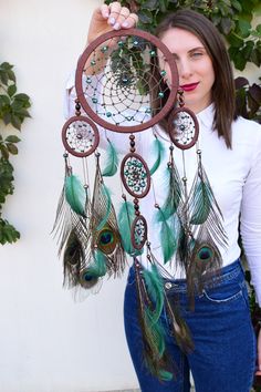 a woman holding up a dream catcher with feathers on it's sides and eyes