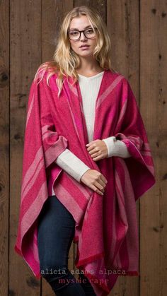 a woman standing in front of a wooden wall wearing a pink and white striped shawl