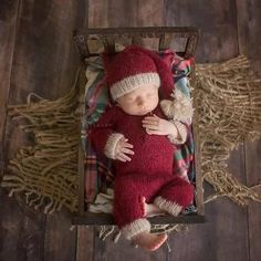 a baby sleeping in a wooden crate with a red hat and mittens on it's head