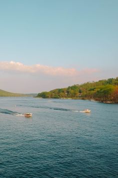 two boats traveling on the water with trees in the background and hills in the distance