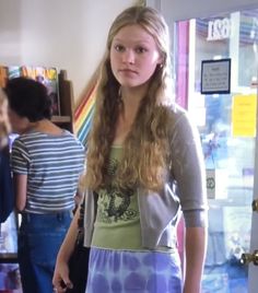 a girl standing in front of a door with her hands in her pockets and looking at the camera