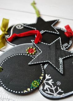 three black ornaments with red and green bows on them sitting on a white tablecloth