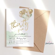 a birthday party card with balloons in gold foil on top of brown envelope and beige envelope