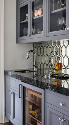 a kitchen with gray cabinets and marble counter tops, wine glasses on the bar top