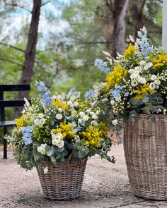 two wicker baskets filled with flowers sitting on top of a dirt ground next to a park bench