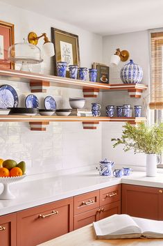 a kitchen with blue and white dishes on the shelves, oranges in vases next to an open book