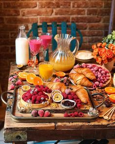 an assortment of fruits and pastries on a tray next to a pitcher of orange juice