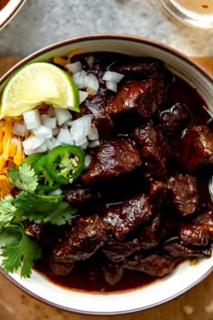 a bowl filled with meat, onions and cilantro on top of a wooden table