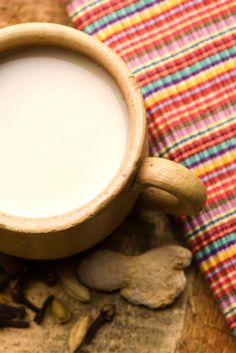 a cup of milk sitting on top of a wooden table next to mushrooms and a plaid cloth