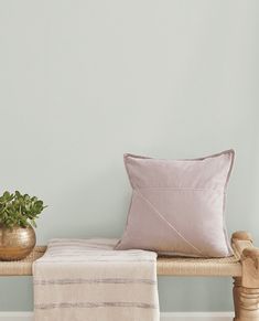 a wooden bench topped with a pillow next to a potted plant and a blanket