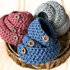 three crocheted baby booties sitting in a basket on a wooden surface with buttons