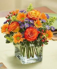 a vase filled with orange and purple flowers on top of a table next to silverware