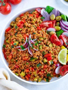 a white bowl filled with rice, tomatoes, onions and cucumbers next to other vegetables