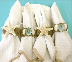 four white towels with starfish and seashells on them, sitting in front of a blue background