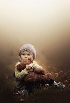 a little boy sitting in the grass holding a teddy bear