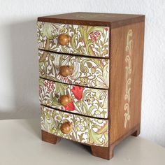 an ornately painted wooden chest of drawers on a white table with a wall in the background