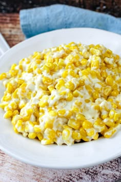 a white plate topped with corn covered in cheese and sauce on top of a wooden table