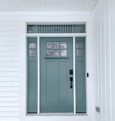 a green front door on a white house with glass panes and sidelights