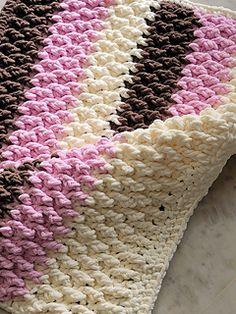 a crocheted blanket laying on top of a white table next to a brown and pink pillow