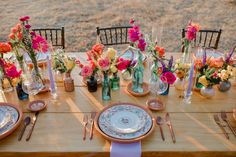 the table is set with plates, silverware and vases filled with colorful flowers