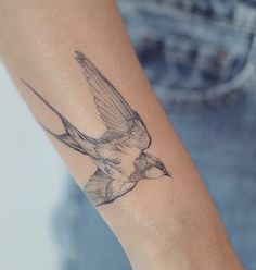 a small bird tattoo on the arm and wrist is shown in black ink, while it appears to be flying