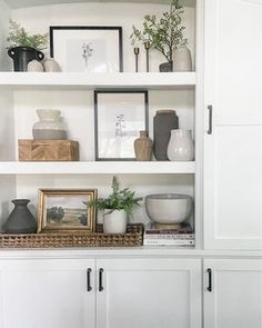 a white shelf with vases and pictures on it in a room that is well decorated