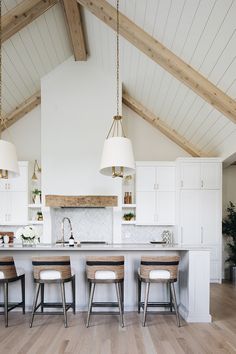 a large kitchen with white cabinets and wooden beams on the ceiling, along with bar stools